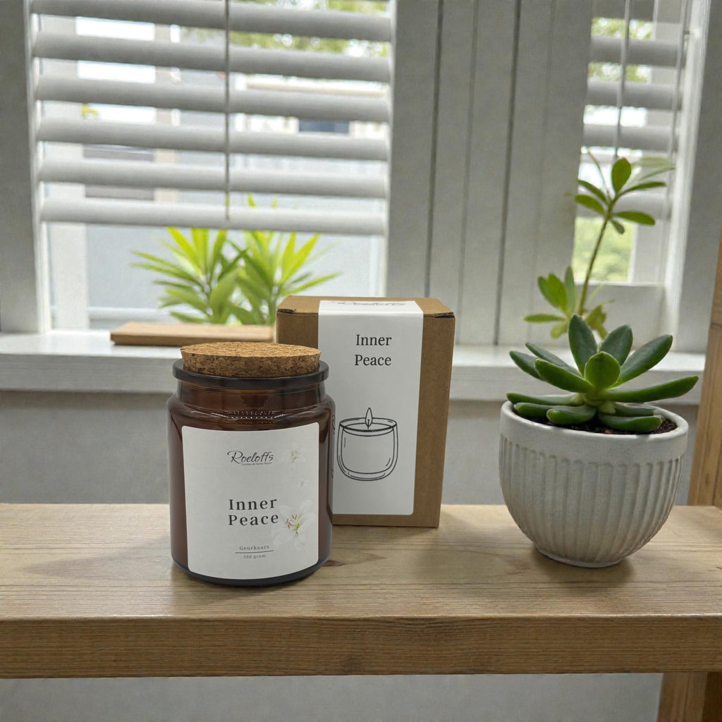 Geurkaars Inner Peace op een tafel, naast een plantenpot en een doos met het label Inner Peace.